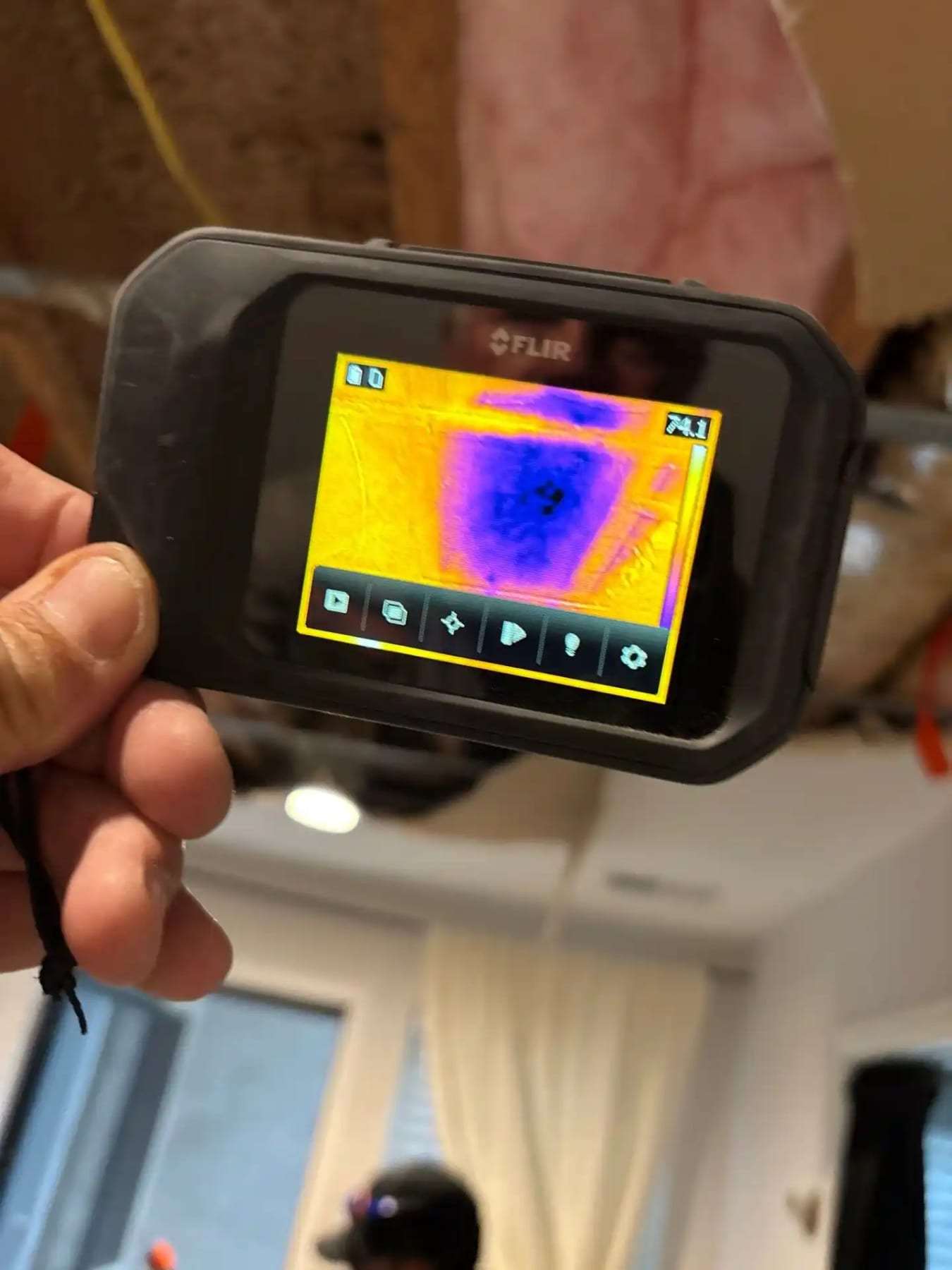 Hand holding a thermal imaging camera showing a cool spot on a wall